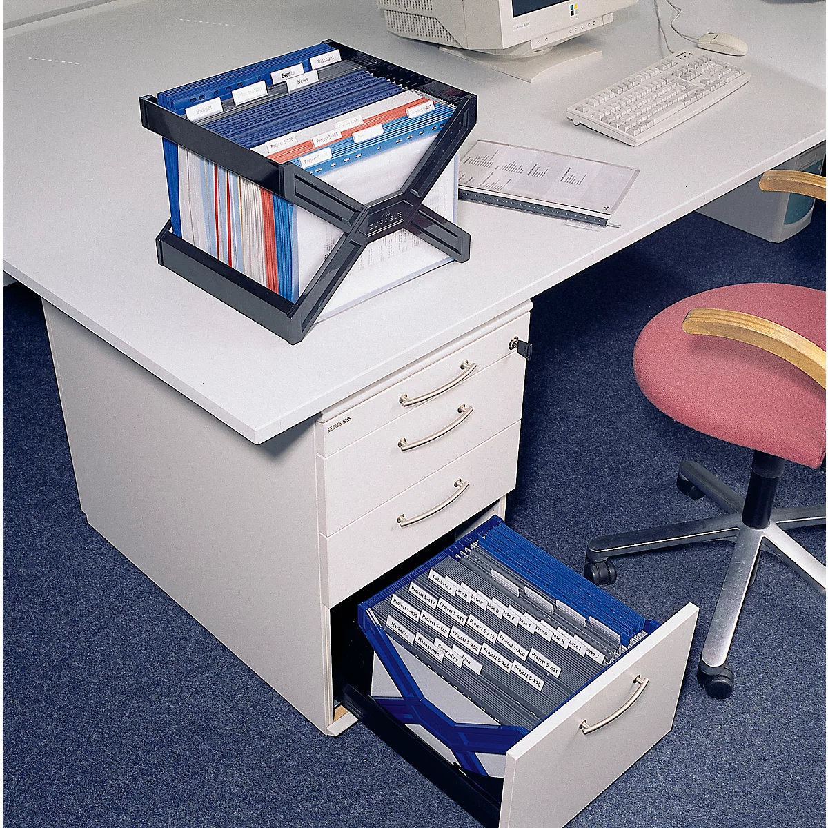 Black file holder with colored file folders on a desk. Drawer open with more files.