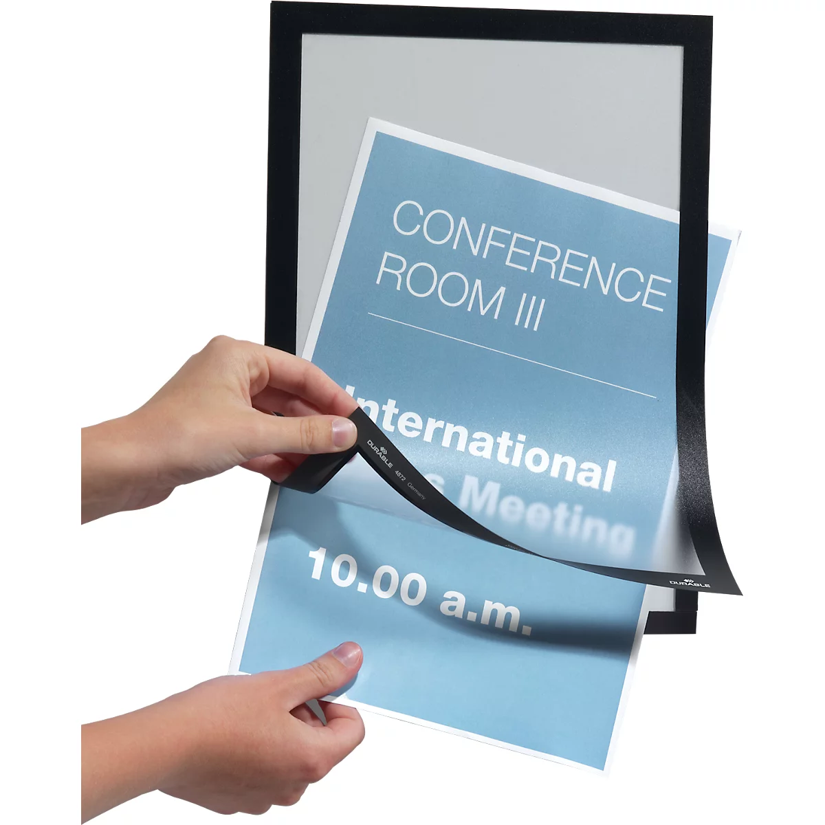 Two hands holding a blue paper with the text "Conference Room III" and "International Meeting". The paper is being removed from a black frame.