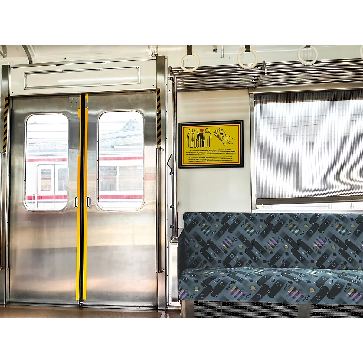 Interieur van een trein met zilverkleurige deuren, een gestoffeerde zitting en een geel waarschuwingsbord aan de muur.