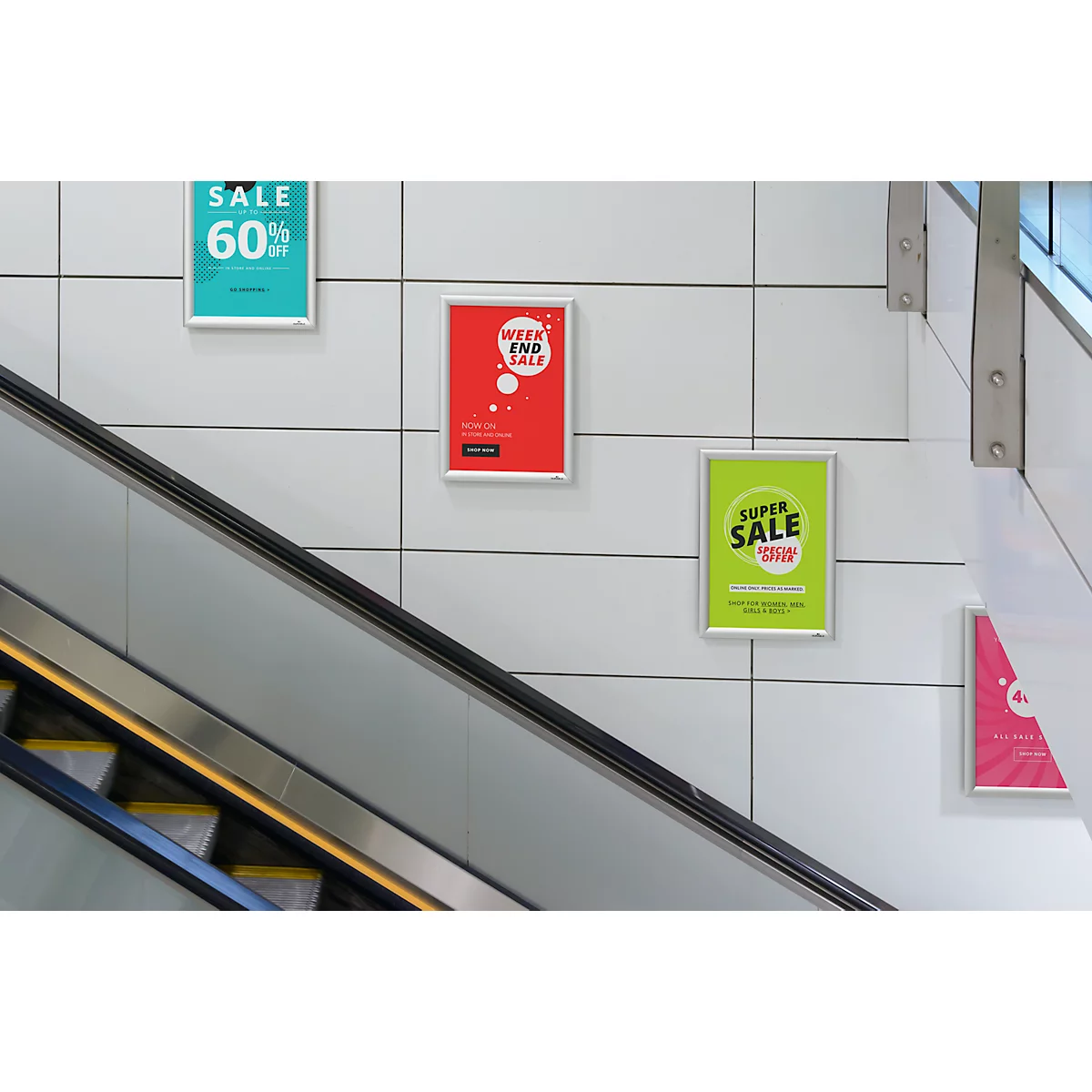 Wand mit Werbeplakaten, eine Rolltreppe im Vordergrund. Die Plakate zeigen 'Sale' Angebote.