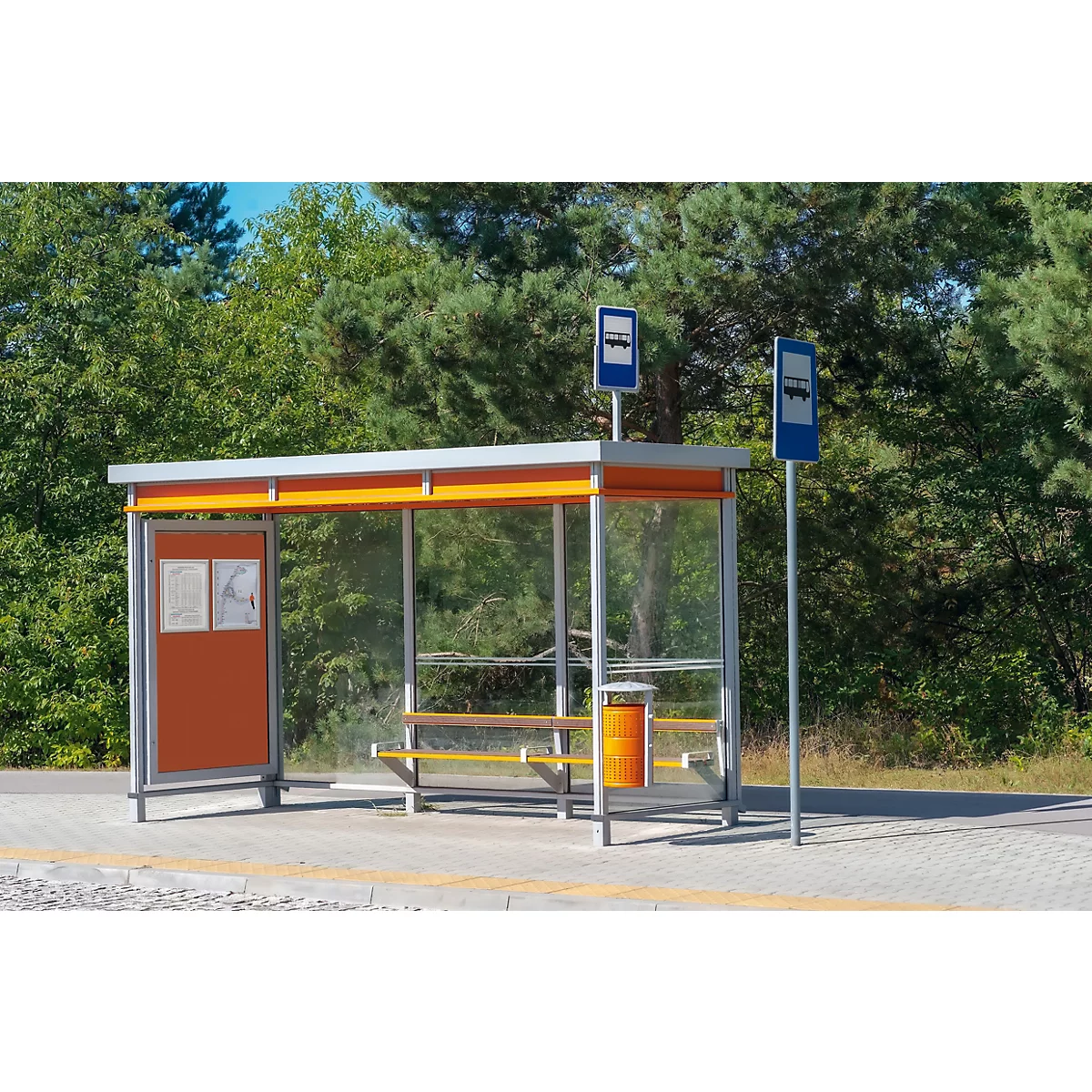 Eine moderne Bushaltestelle mit orangefarbenen Elementen und Glaswänden vor einem Waldrand.