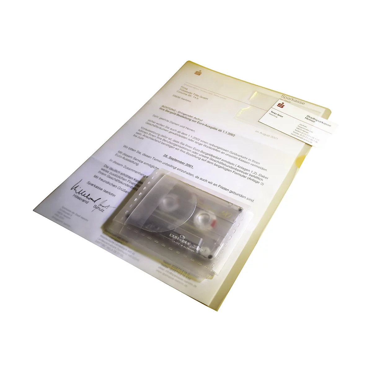 Eine transparente Sparkassen-Mappe mit Geschäftsbrief, Visitenkarte und einer eingesteckten Musikkassette.