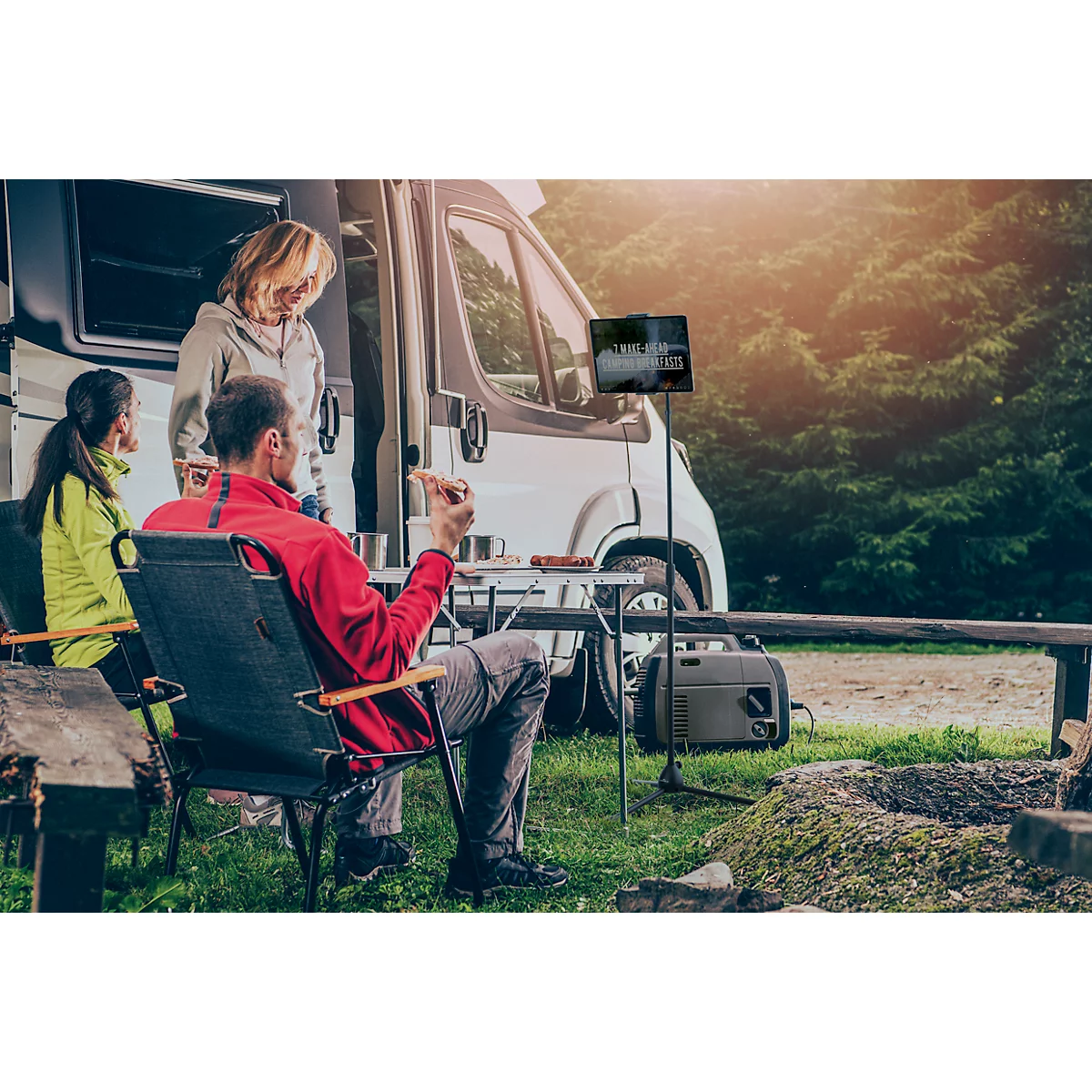 A family relaxing in front of a camper. The man is sitting in a chair, the others are standing.