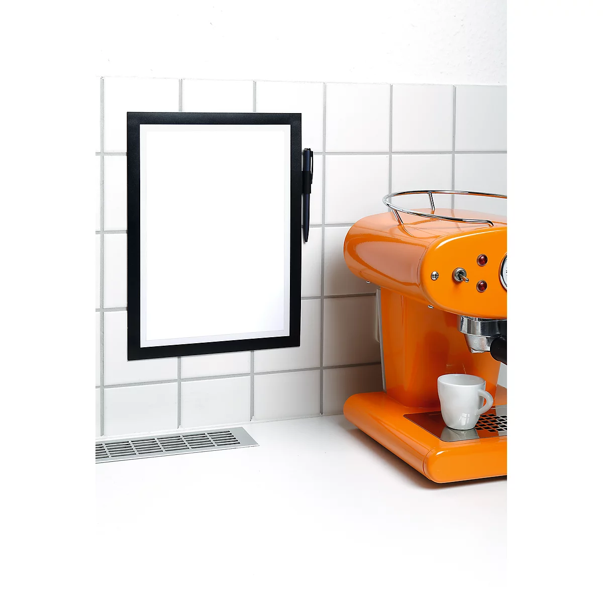 Orange coffee machine with white cup, next to a black board hanging on white tiles.
