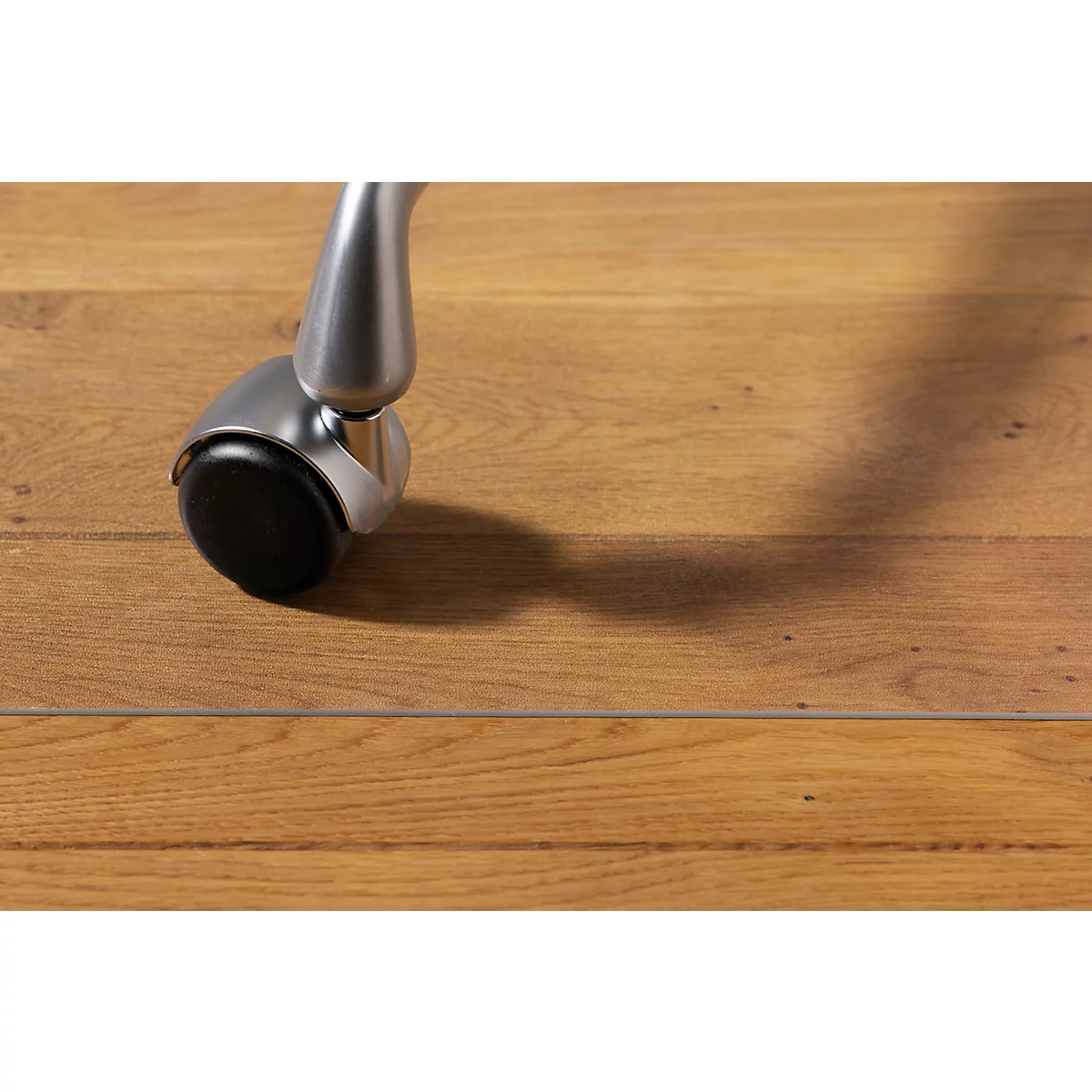 Primer plano de una rueda de silla sobre suelo de madera, proyectando una sombra.