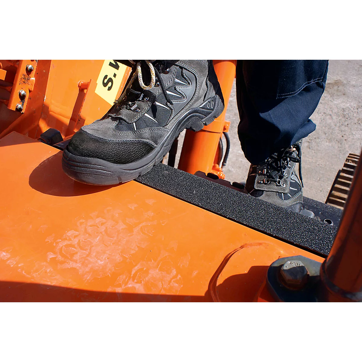 Two feet on an orange machine. Black boots stand on a black non-slip surface. The machine says "S.M."