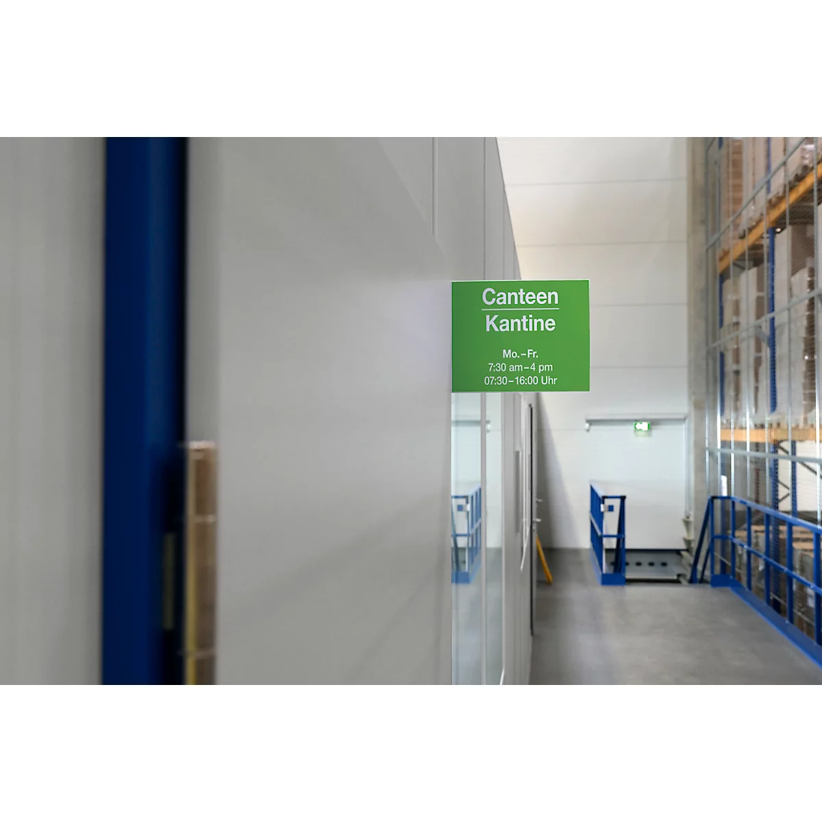 Groen kantinebord met openingstijden. Op de achtergrond een gang en magazijnstellingen.