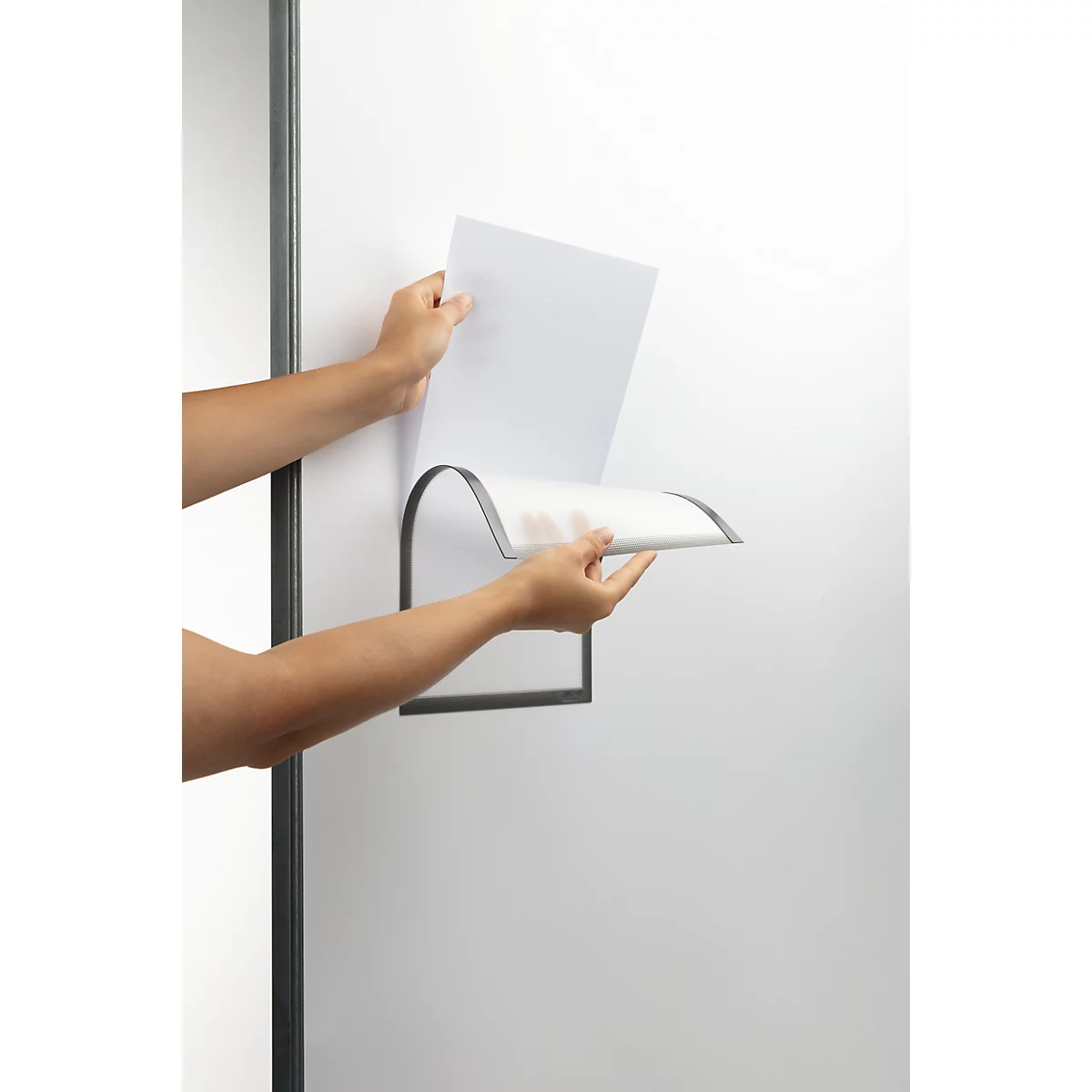 Handen plaatsen papier in een aan de muur gemonteerde houder. De houder is van metaal en hangt aan een witte muur.