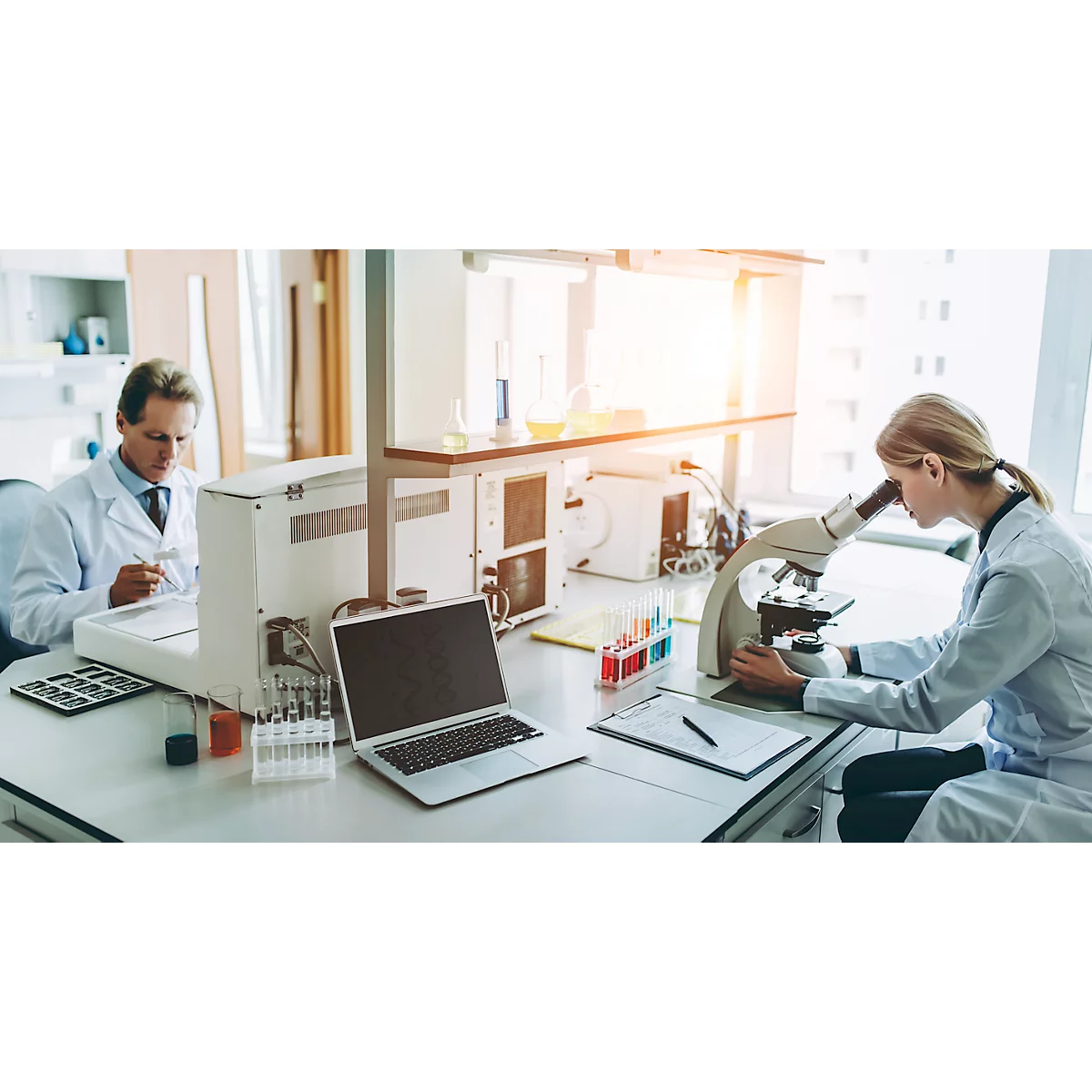 Twee wetenschappers die in een laboratorium werken aan microscopen en andere apparatuur.