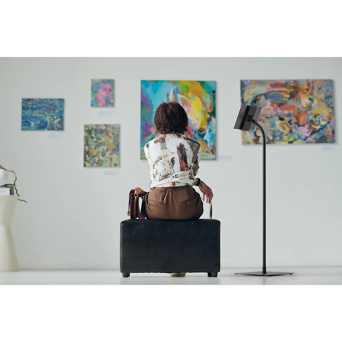 Een persoon beschouwt schilderijen in een galerie. Ze zitten op een kruk en kijken naar de muur met verschillende kunstwerken.