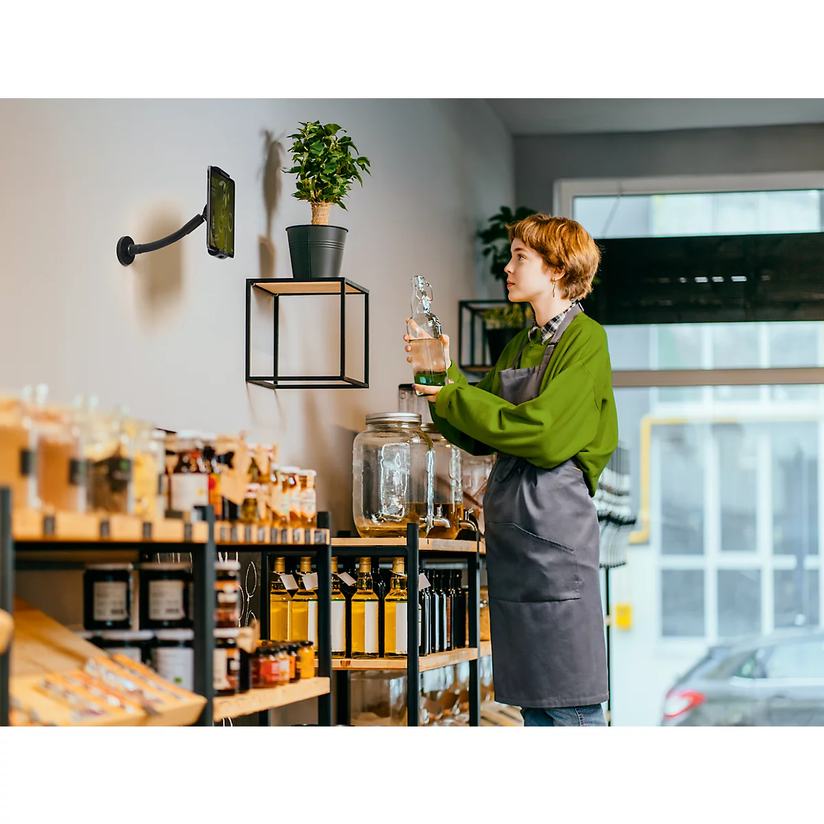 Jonge vrouw houdt glazen fles vast in duurzame winkel, draagt een schort.