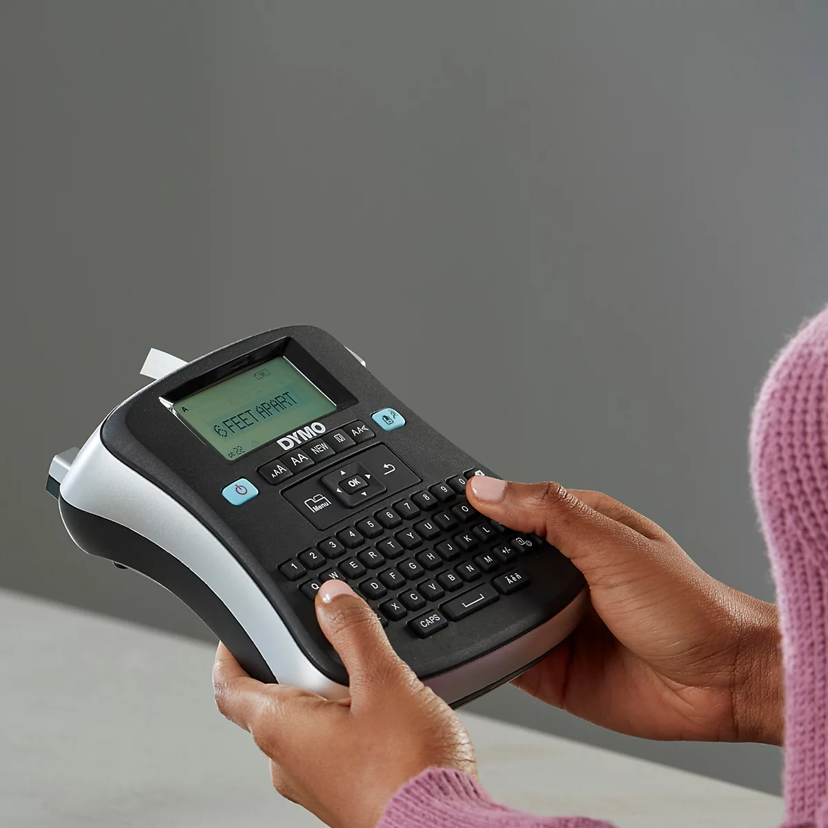 Persoon typt op een zwarte DYMO-labelmaker met '6 FEET APART' op het display.
