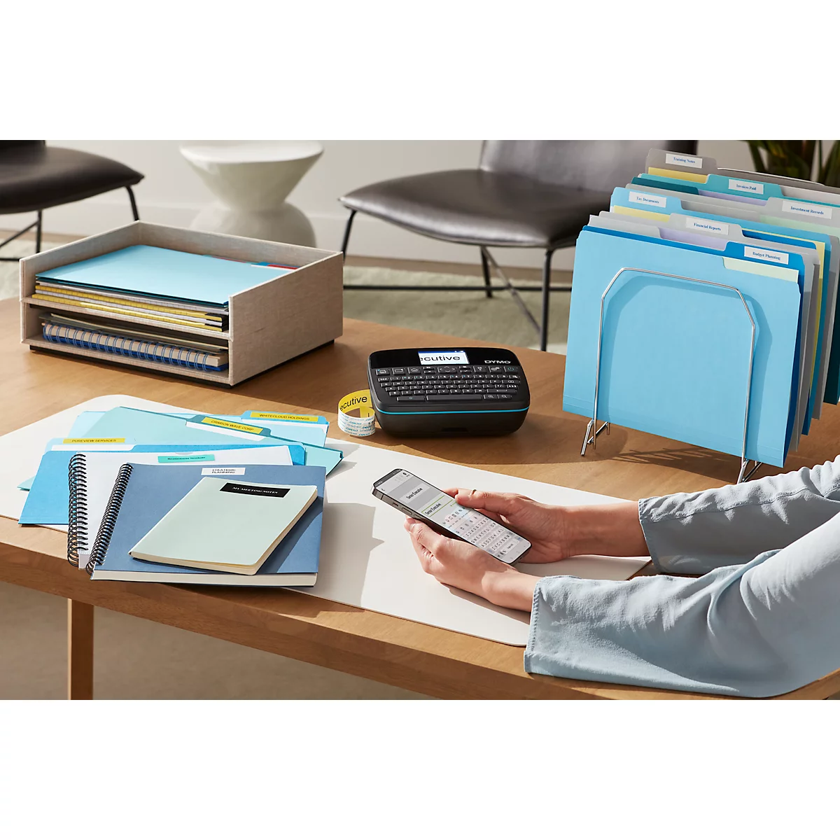 Person mit Smartphone beschriftet Etiketten, Notizbücher, Ordner und Ordnerständer.