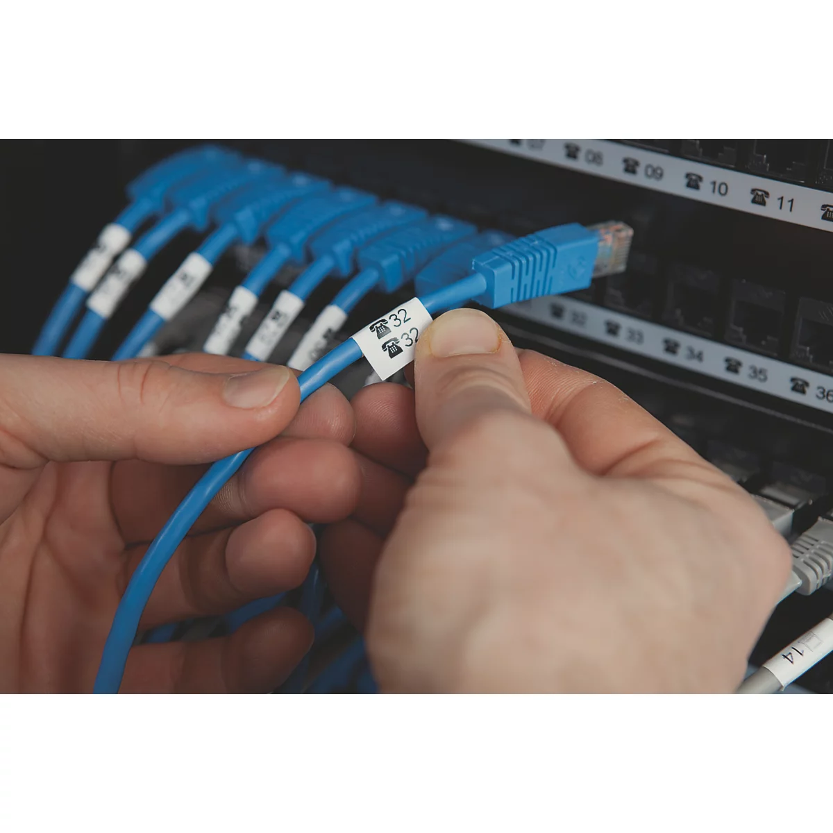 Hände halten ein blaues Netzwerkkabel mit einem Etikett, das ein Telefonsymbol und die Zahl 32 zeigt.