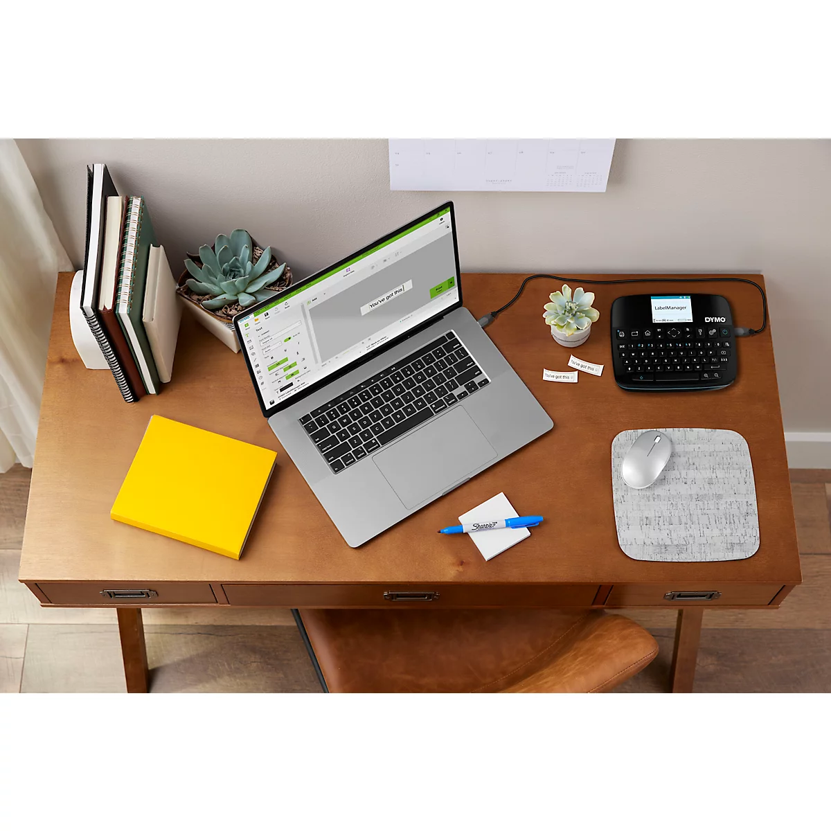 Bovenaanzicht van een bureau met laptop, labelmaker, notities, muis en notitieboek.