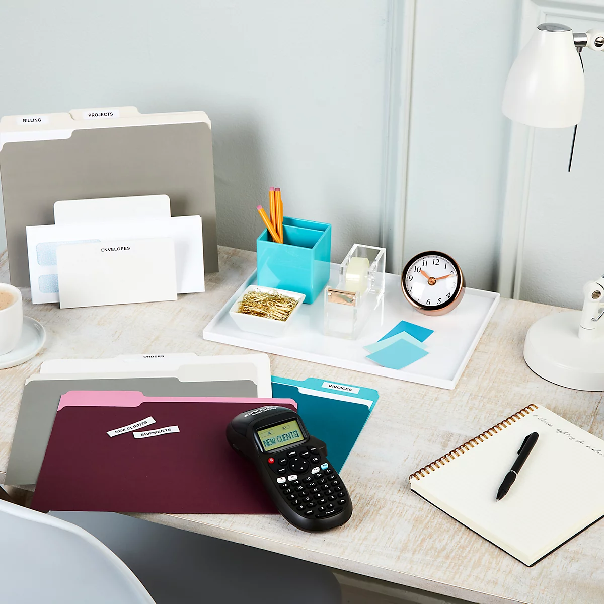 Bureaublad met ordners, pennenbakje, klok en labelmaker. Het label zegt 'Nieuwe klanten'.