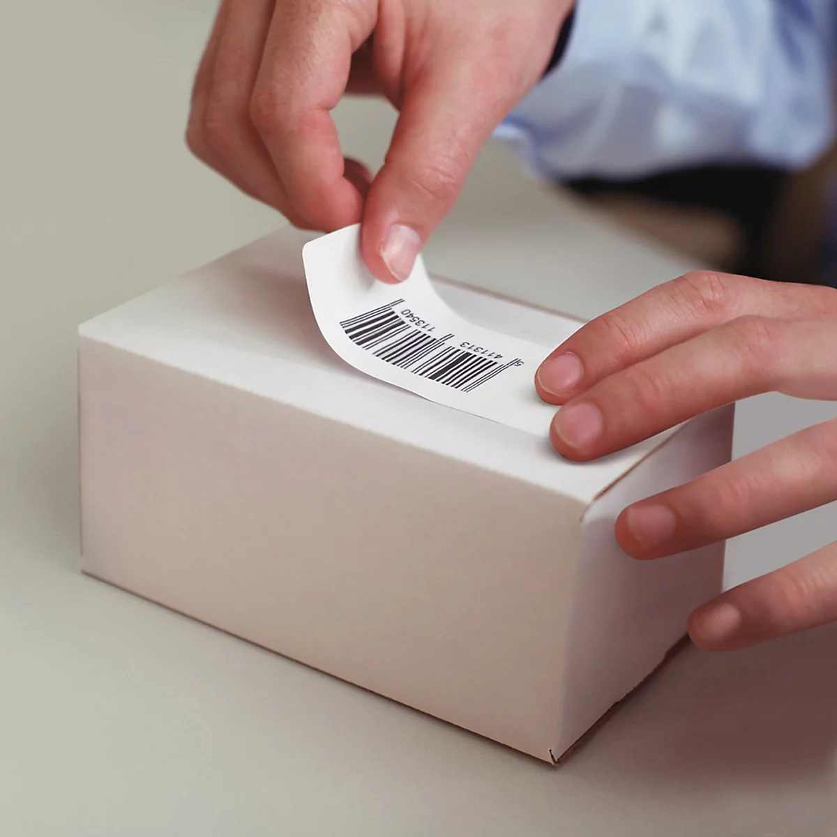 Hände kleben einen Barcode-Aufkleber auf einen weissen Karton.