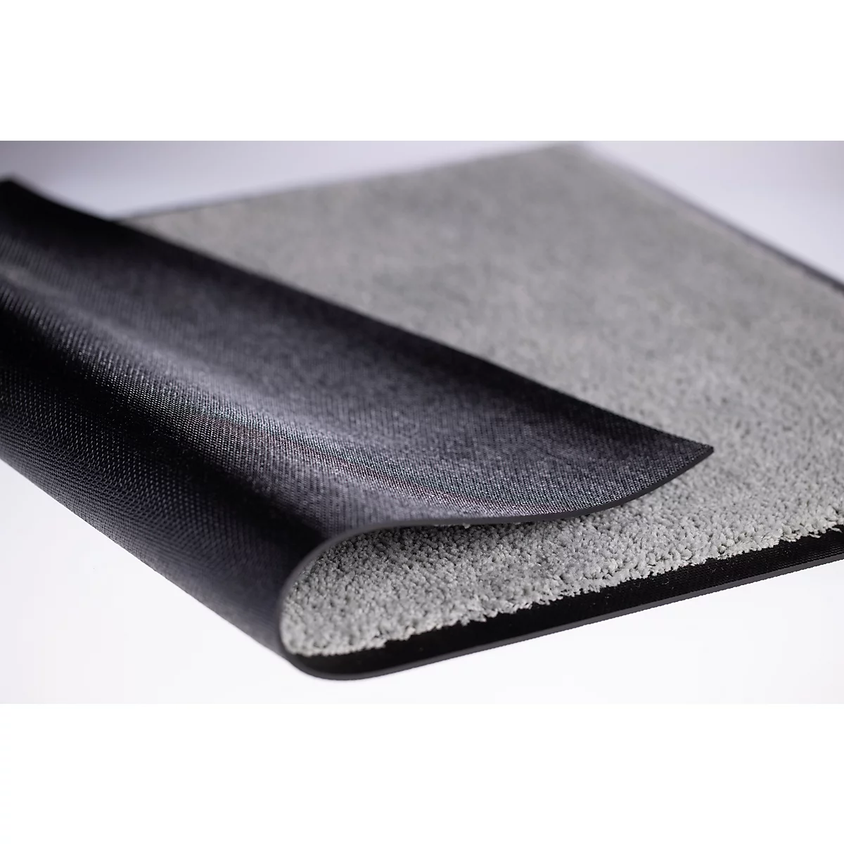 Een tapijt met een grijze pooloppervlakte en een zwarte, antislip rubberen achterkant, lichtjes omgeklapt.