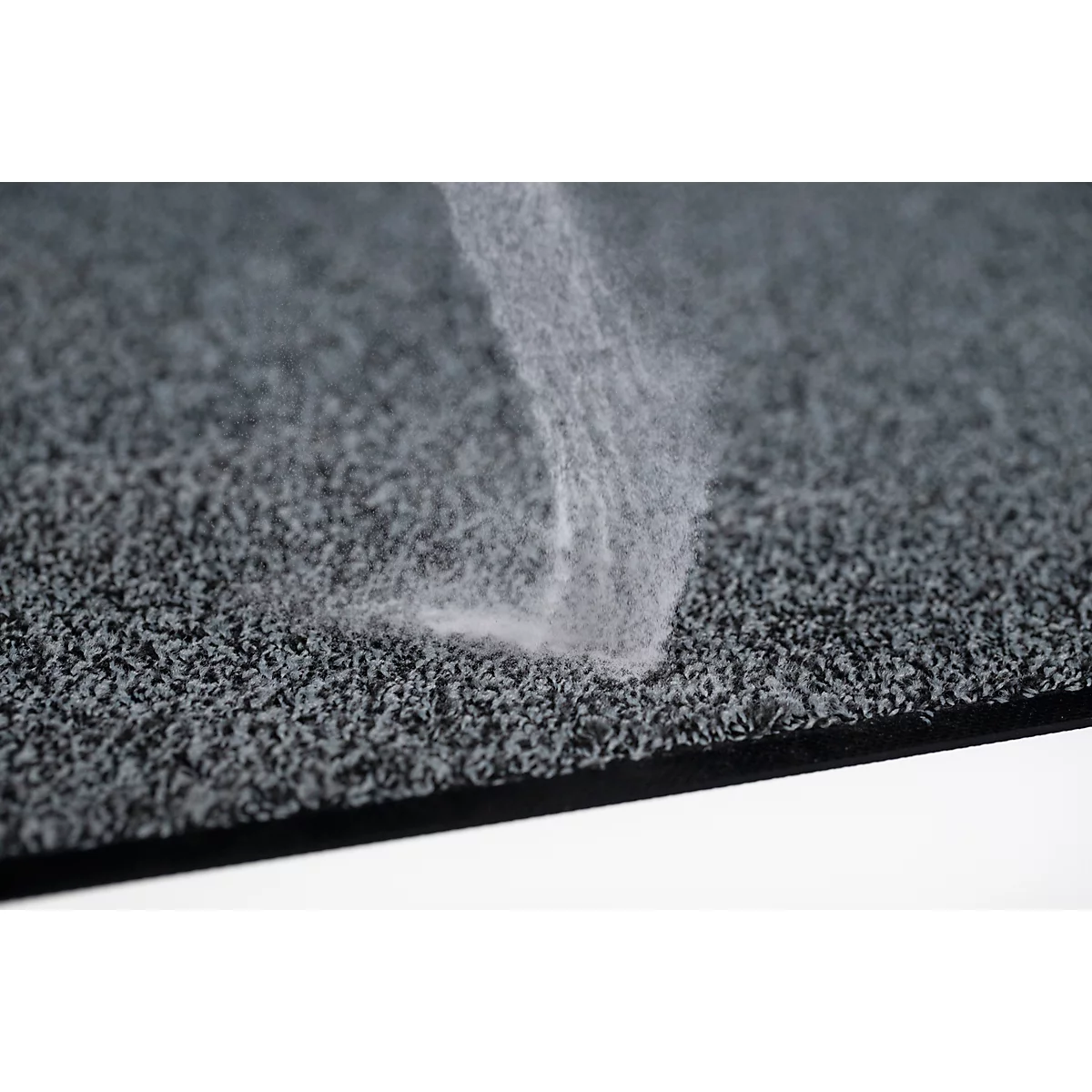 Primer plano de una alfombra gris texturizada con polvo blanco o fibras depositándose en forma de remolino.