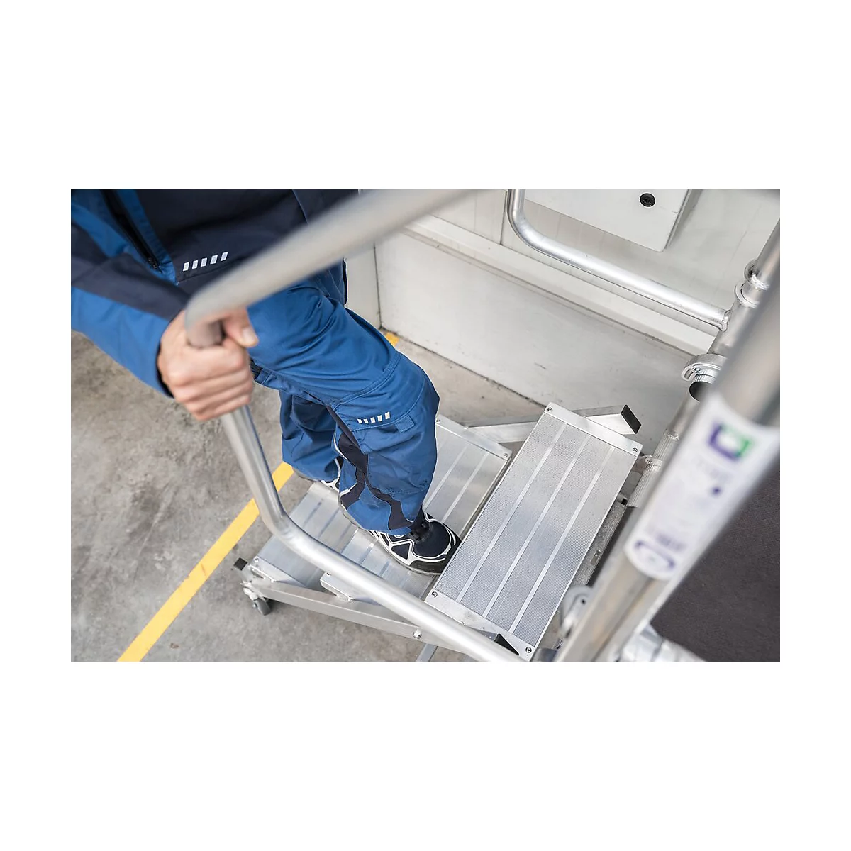 Personne montant une échelle argentée. Pantalon bleu et chaussures noires.