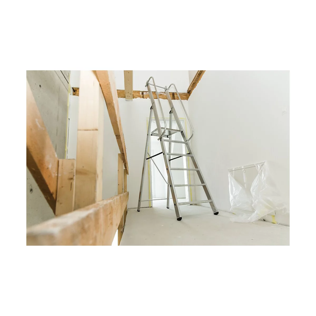 Un escabeau se trouve dans une pièce en construction. Construction en bois au premier plan, fond blanc. Porte et feuille de plastique en arrière-plan.