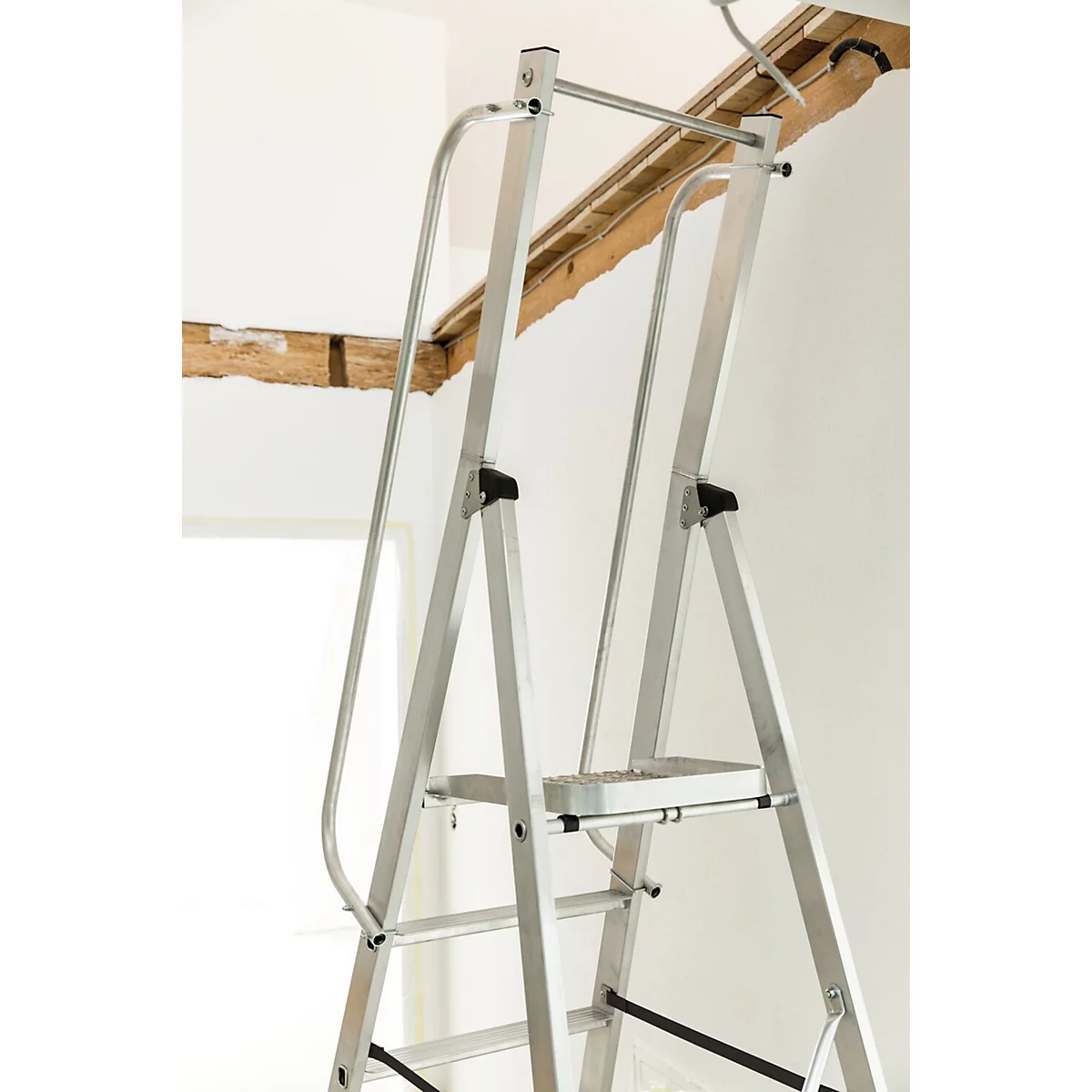 Échelle en aluminium devant un mur blanc, poutres en bois en arrière-plan.