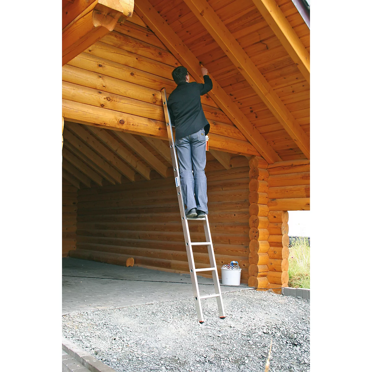 Personne sur une échelle peignant le plafond en bois dans une maison en bois.