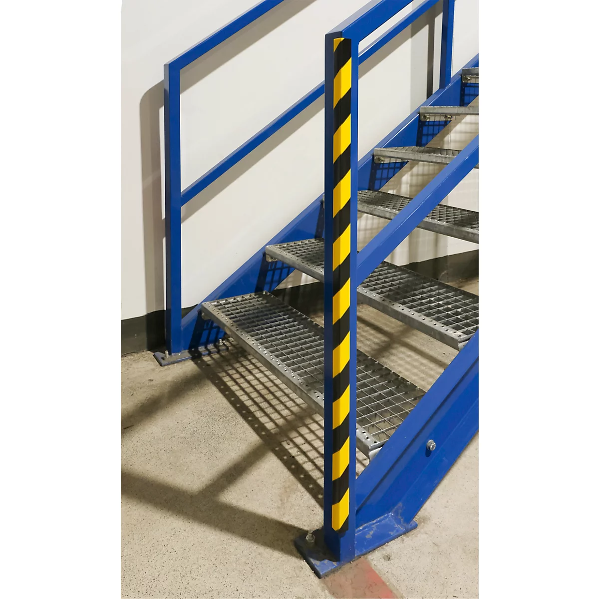Blaue Metalltreppe mit gelb-schwarzem Warnstreifen. Geländer, Gitterstufen, Winkelstahl. Betonboden.