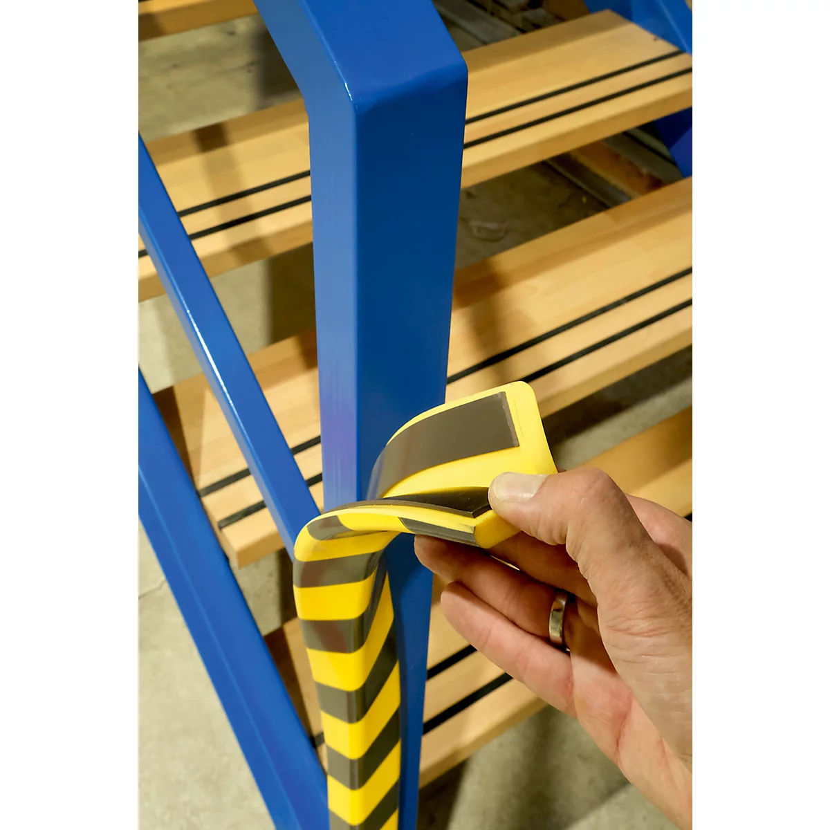 Blaue Treppe mit Geländer und Holzstufen, zusätzlich gelb-schwarzer Kantenschutz.