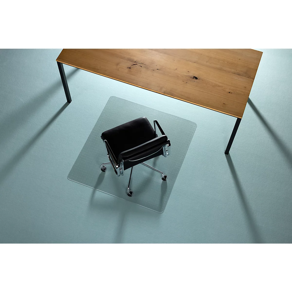 Bureaustoel op transparante vloerbeschermingsmat onder een houten bureau.