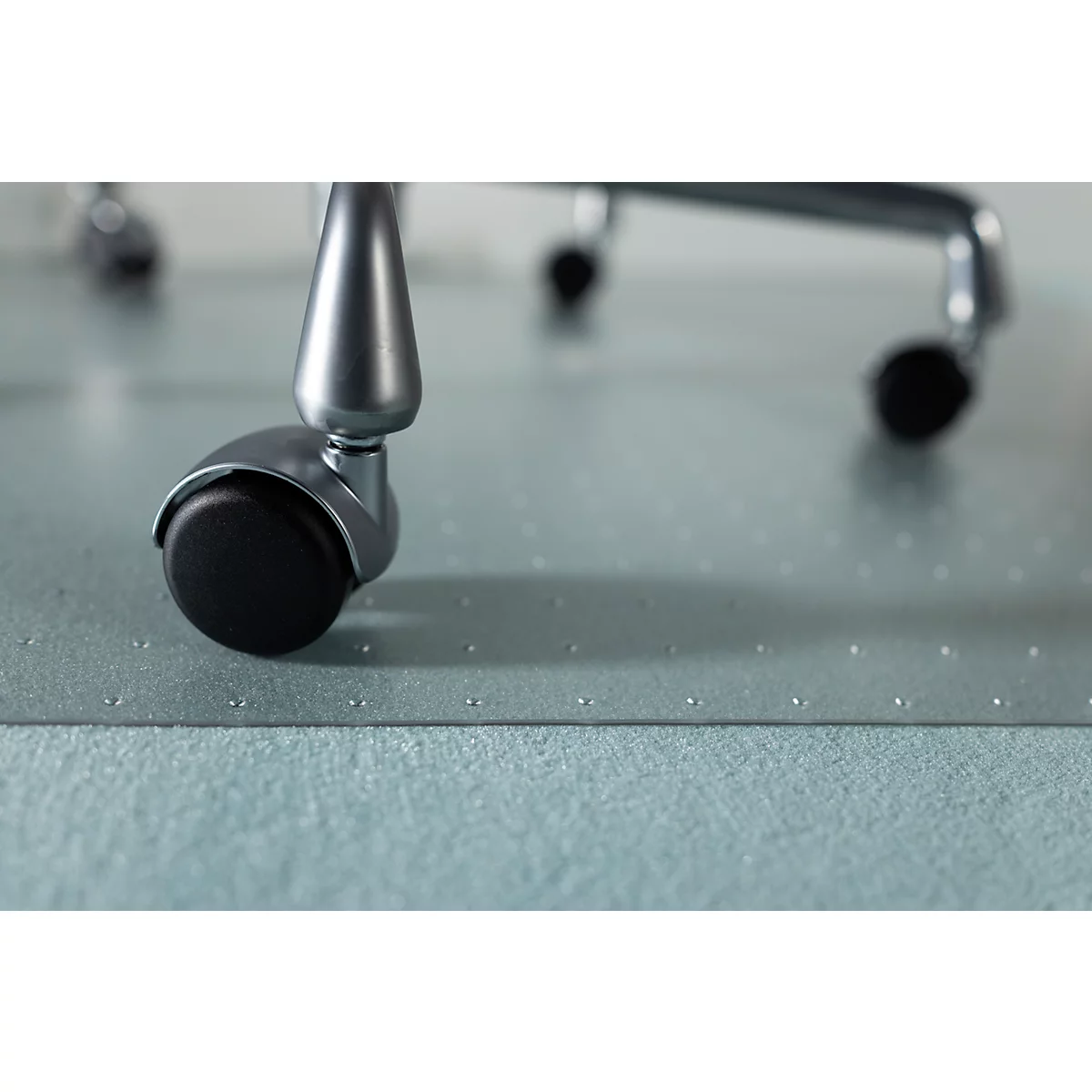 Close-up van een stoelwiel met zwart rubber op een blauwe, gestippelde mat.