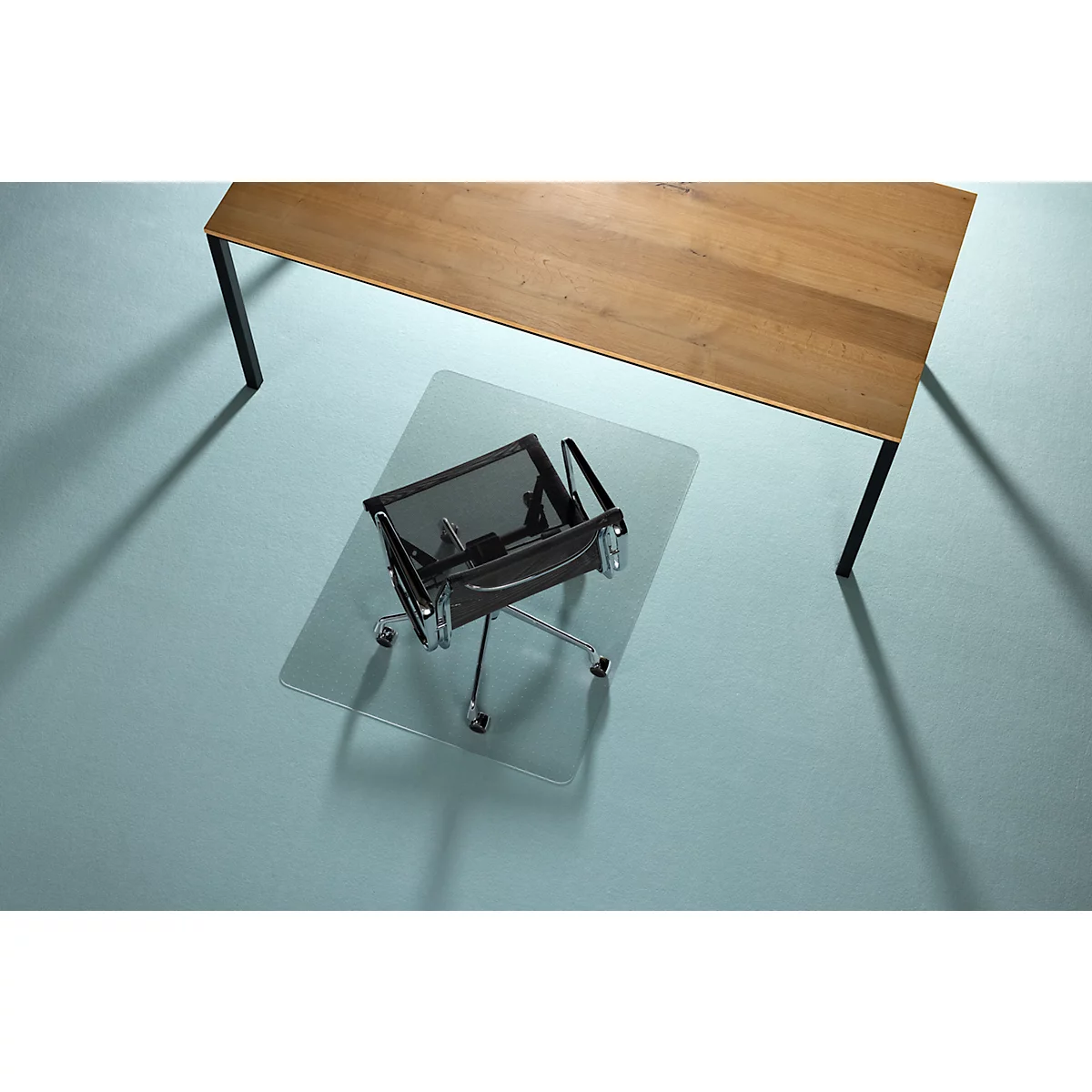 Een bureaustoel staat op een transparante vloerbeschermingsmat onder een houten tafel. De achtergrond is lichtblauw.