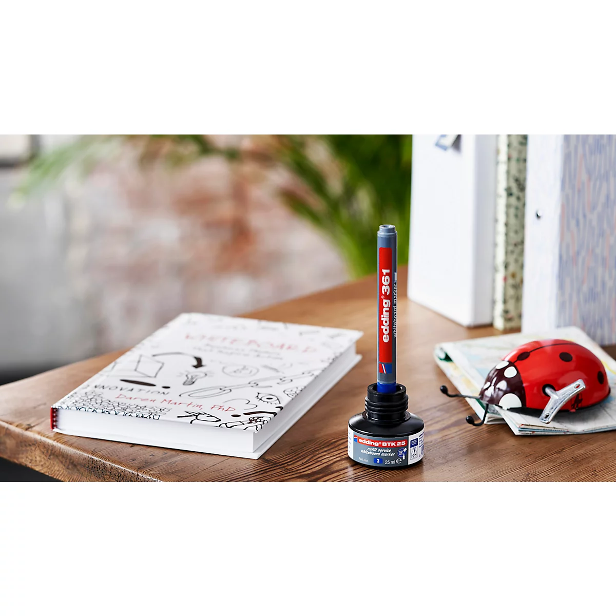 Een pen staat in een inktpot naast een boek en een lieveheersbeestjesdecoratie.