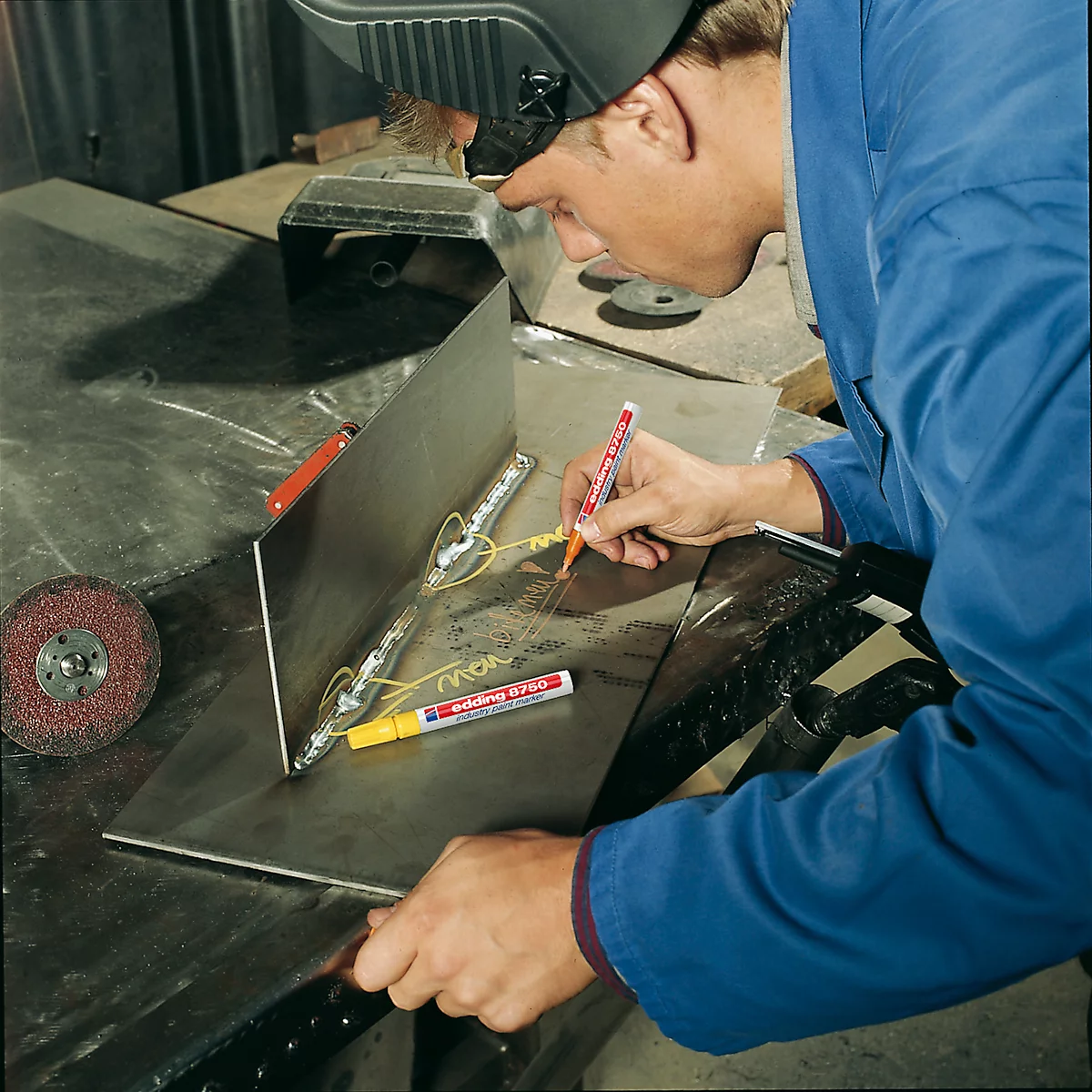 A man in work clothes marks metal parts with a pen for welding.