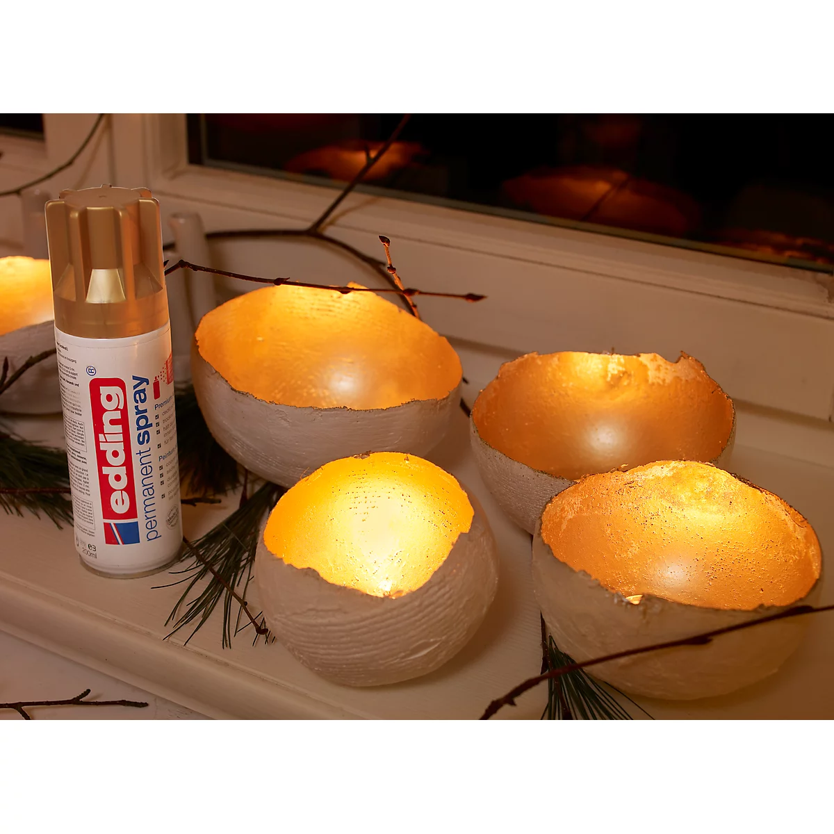 Vier gouden kaarsen in crèmekleurige kommen, naast een gouden Edding permanente spuitbus.