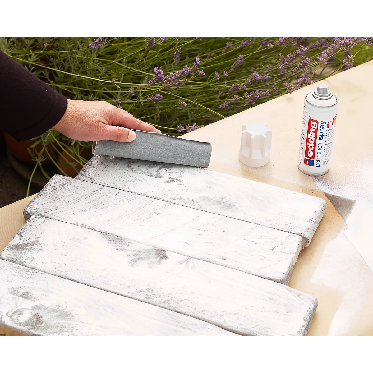 Persoon die houten planken schuurt; daarnaast een spuitbus en een deksel.