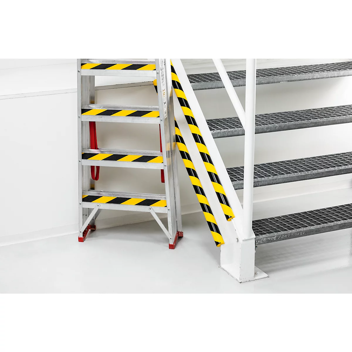 Gray step ladder and steel staircase with warning markings. The step ladder stands on a red base and has yellow and black stripes.