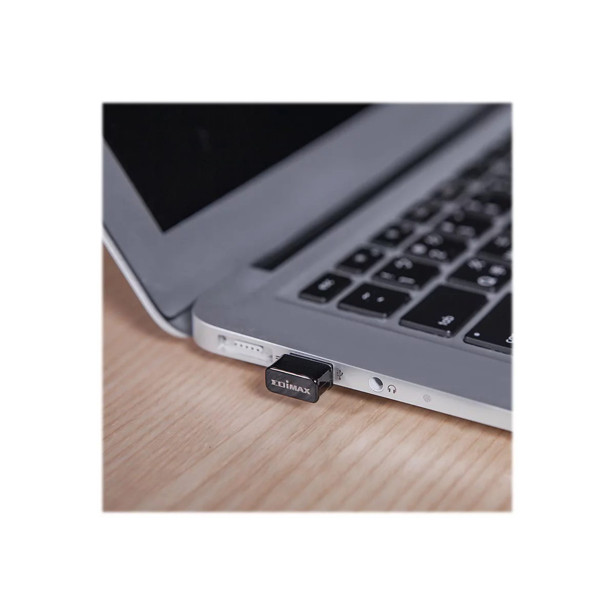 Schwarzer USB-Stick steckt in einem silbernen Laptop. Auf dem Stick steht EDIMAX. Das Laptop liegt auf einem Holzbrett.