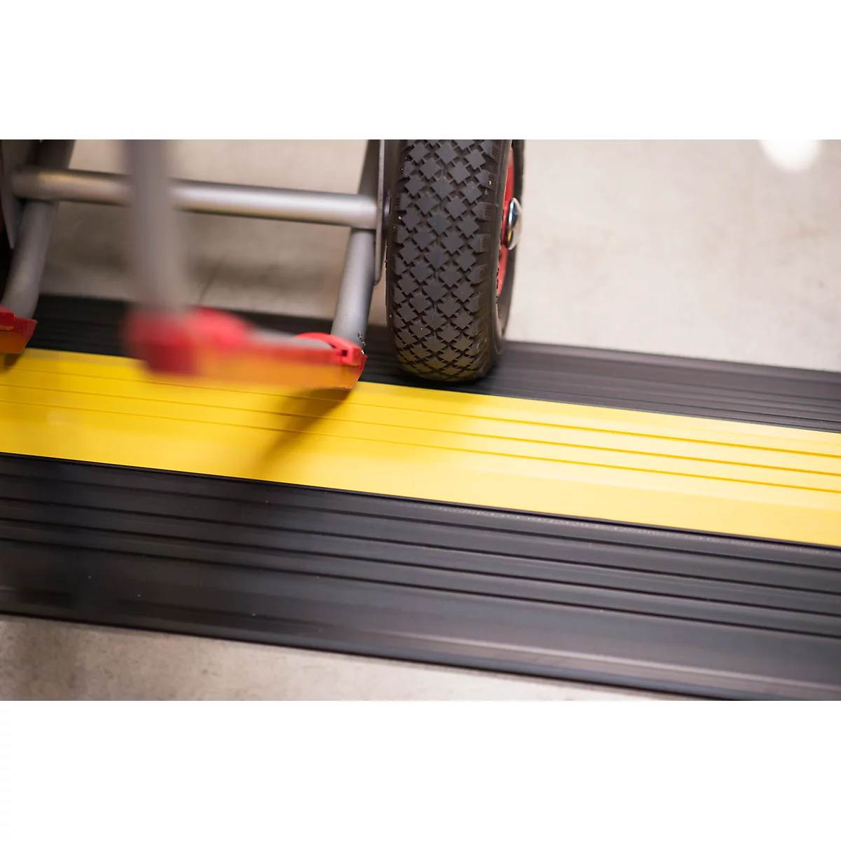 Close-up of a ramp with a yellow stripe and a wheelchair wheel. The ramp is black and the wheel has red accents.