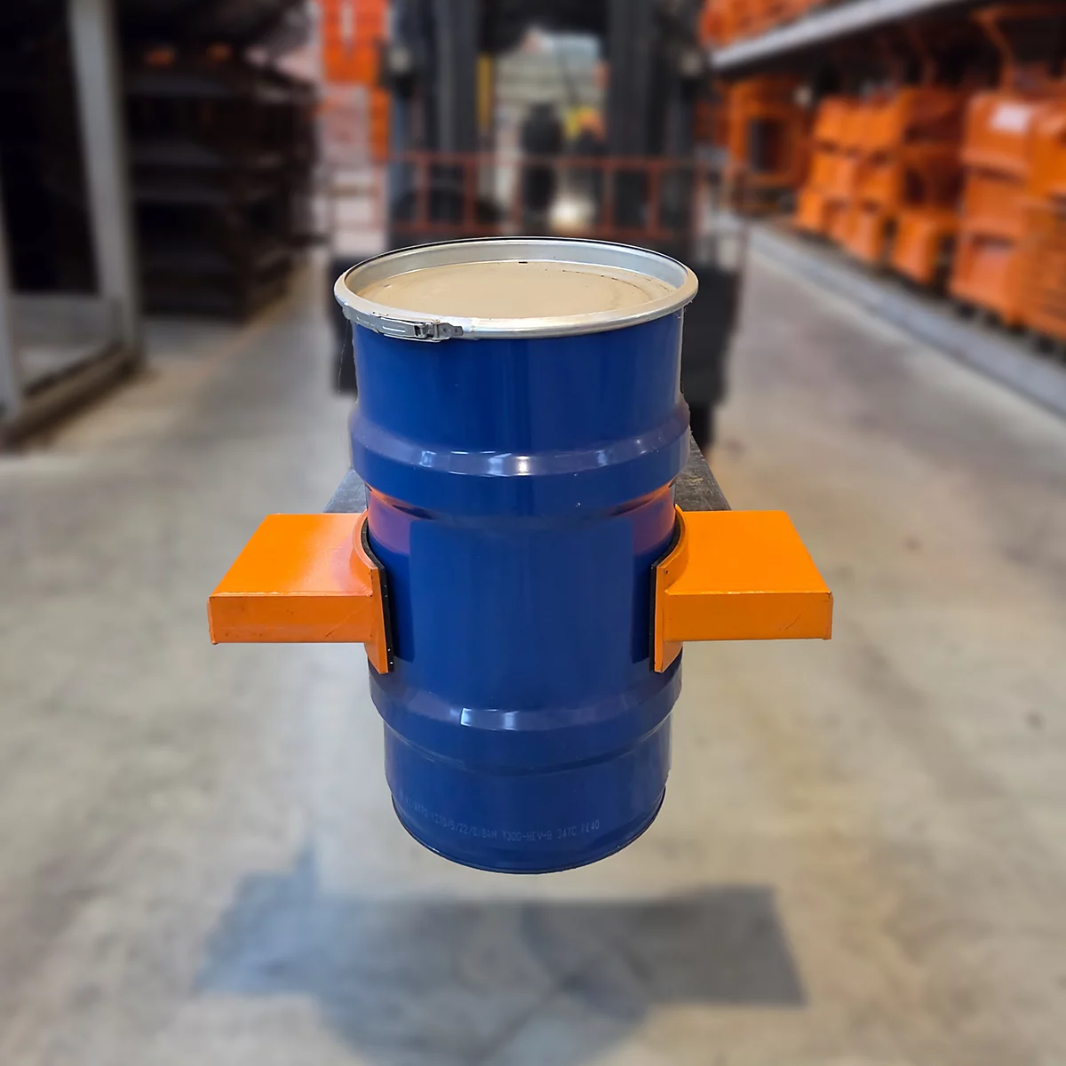 Blauer Metallfass auf orangefarbenen Halterungen, von einem Gabelstapler gehalten.