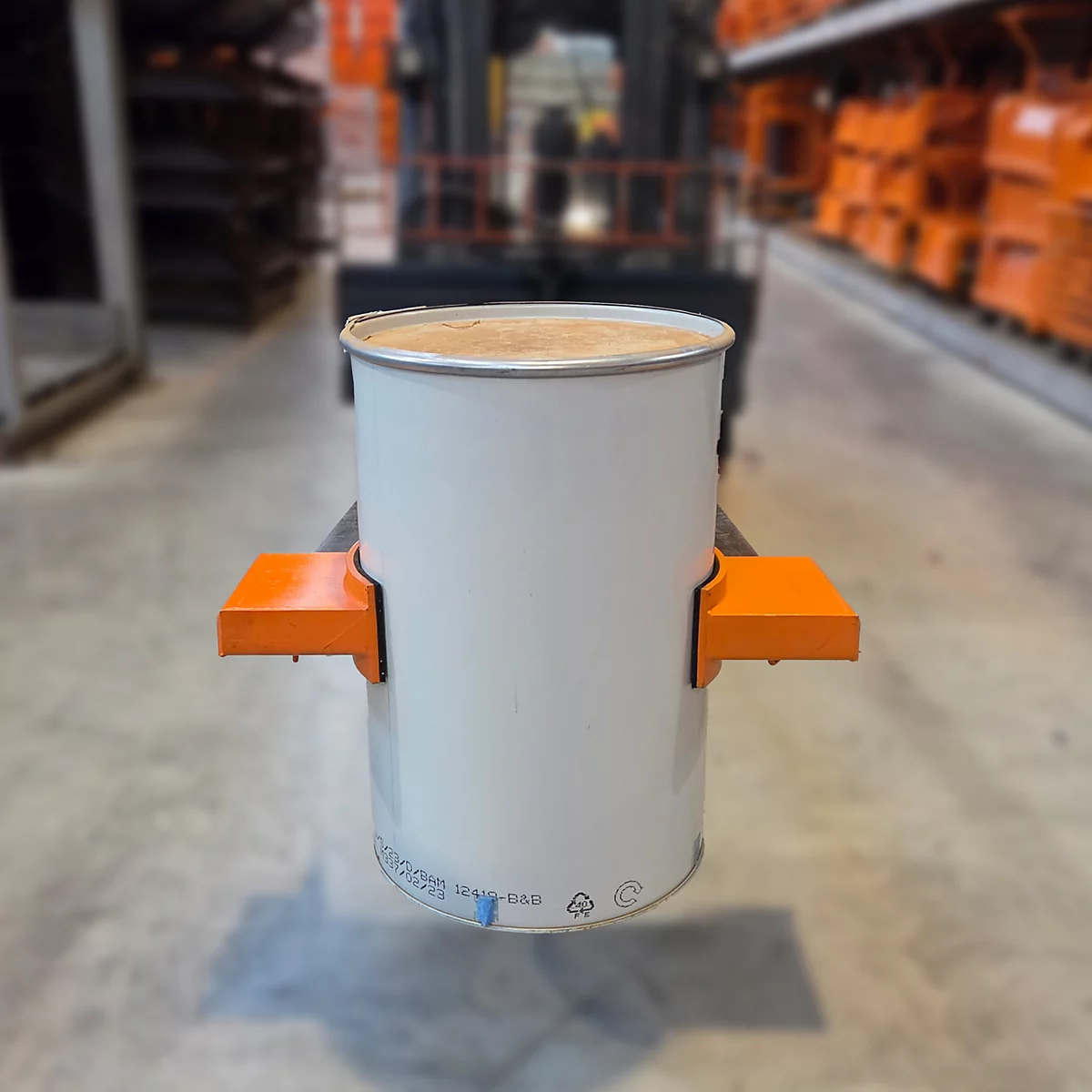 Weißer Fassbehälter wird mit Gabelstapler transportiert. Orangefarbene Halterungen fixieren den Behälter. Lagerhallen-Hintergrund.