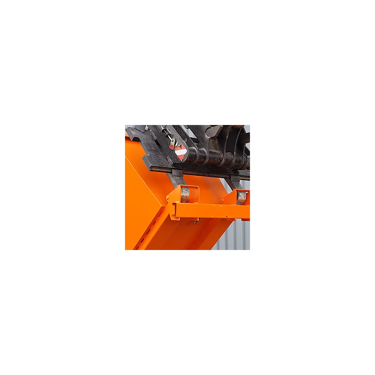 Detailaufnahme einer orangefarbenen Baggerschaufel mit schwarzen Metallteilen, darunter ein rotes und weißes Warnschild.