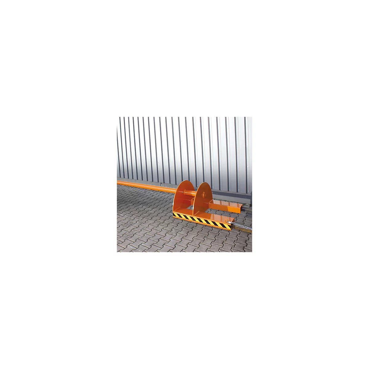 Ein orangefarbener Teppichdorn für Gabelstapler steht auf einem Pflastersteinboden vor einer Metallwand.