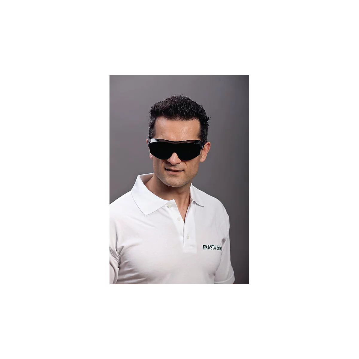 Un homme aux cheveux noirs porte des lunettes de sécurité et un polo blanc. Le polo porte l'inscription 'EKASTU Safety'.