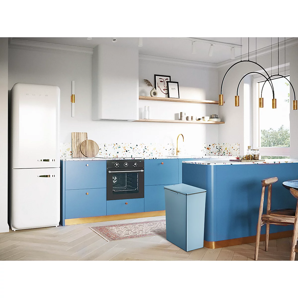 Moderne Küche mit blauer Küchenzeile, weißem Kühlschrank und Mülleimer. Der Raum ist hell und stilvoll eingerichtet.