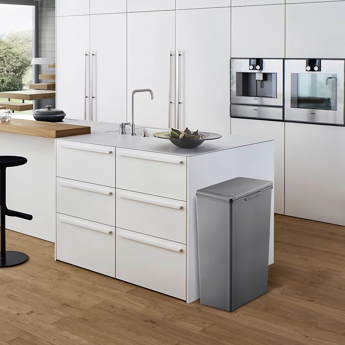 Cuisine moderne avec îlot de cuisine, poubelle grise, armoires blanches, plancher en bois.
