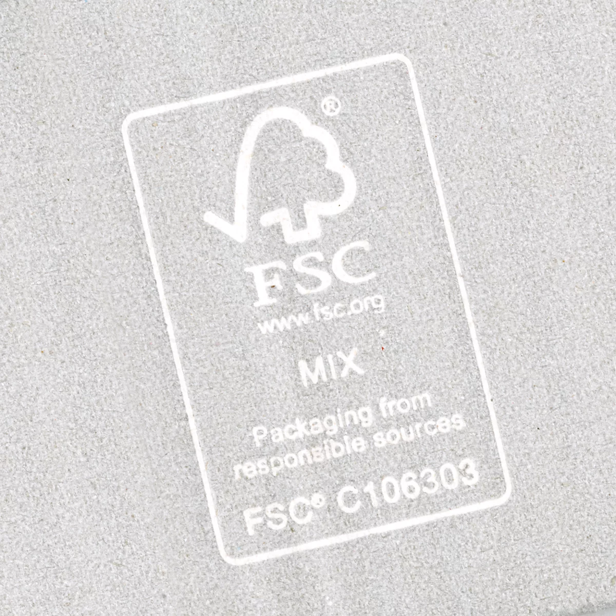 Transparante FSC-sticker op een grijze, gestructureerde achtergrond. De sticker toont een boomlogo en tekst.