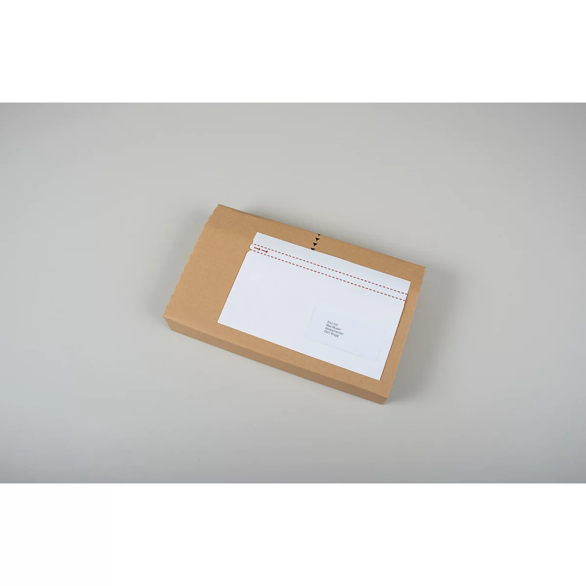 Une boîte d'expédition marron avec une enveloppe blanche posée dessus.