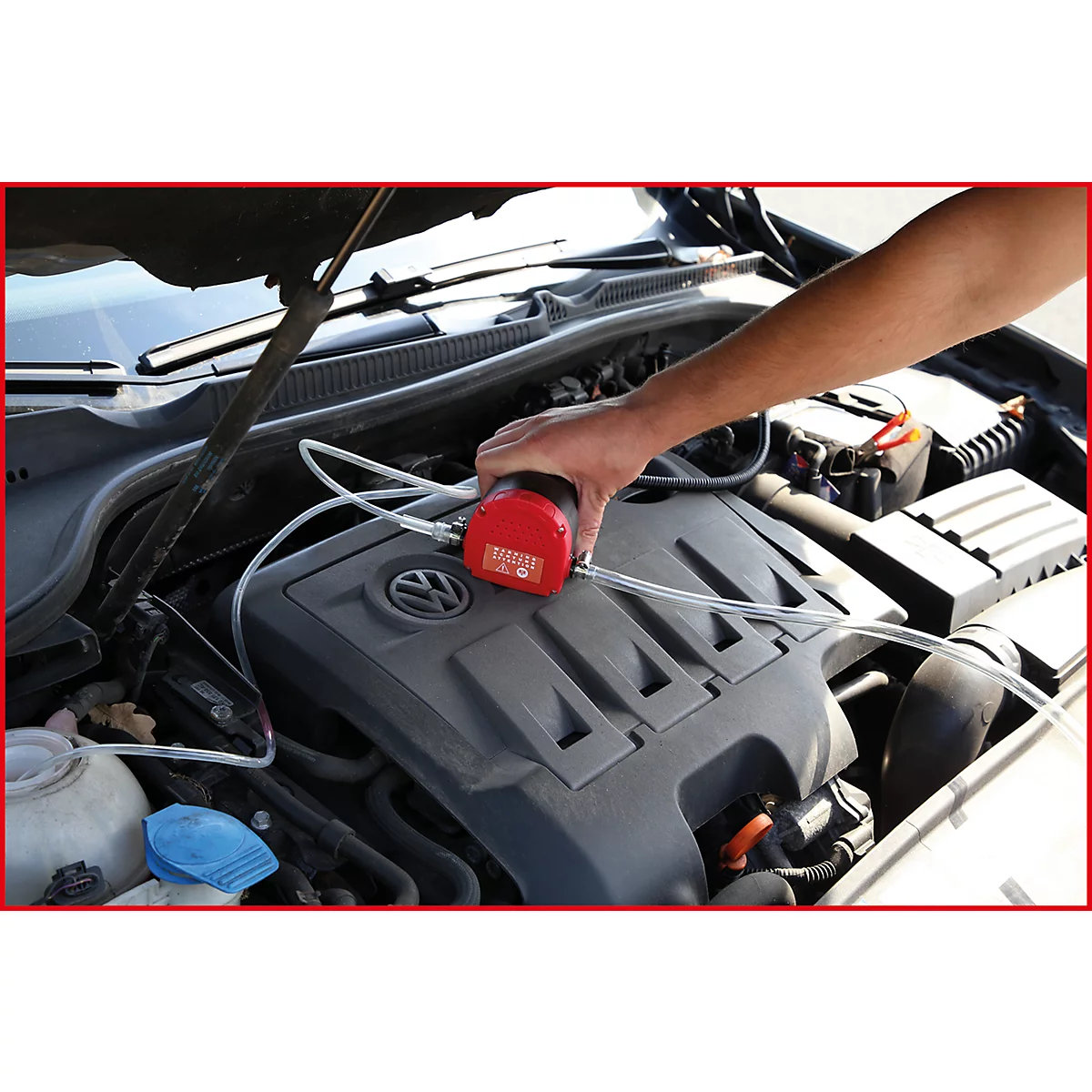 Hand hält rotes Gerät über Motor. Schläuche sind angeschlossen. Volkswagen-Logo.