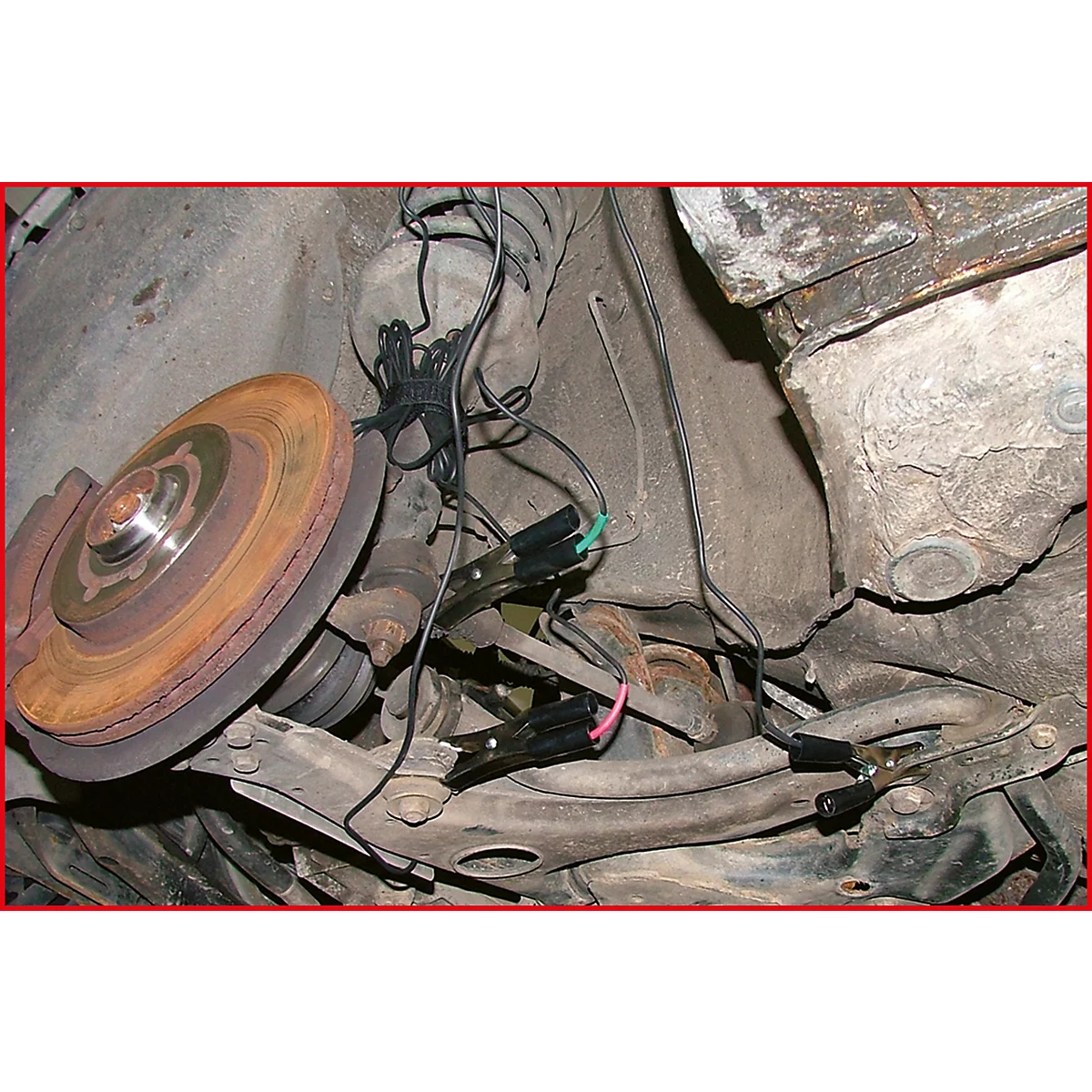 Nahaufnahme einer Fahrzeugaufhängung, Bremsanlage und Kabeln mit Klemmen. Rostiger Bremsscheibe im Fokus.
